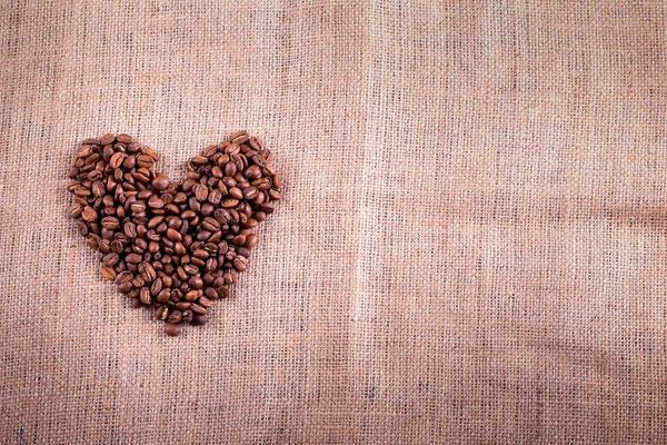 Corazón con granos de café tostados en el fondo de arpillera — Foto de Stock