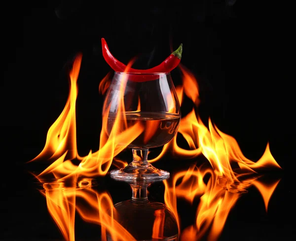 Piment fort dans un ballon de cognac avec un feu sur fond noir — Photo