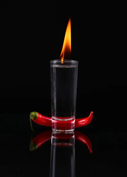 Hot chili pepper in a shot  glass with a fire on a black backgro — Stock Photo, Image