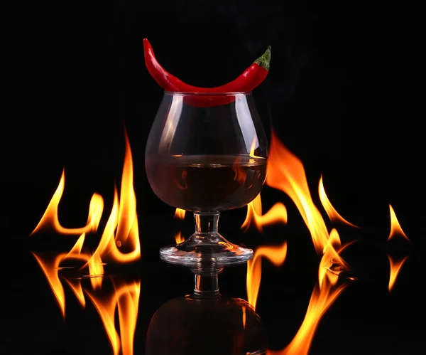 Scharfe Chilischote in einem Cognac-Ballon mit Feuer auf schwarzem Hintergrund — Stockfoto