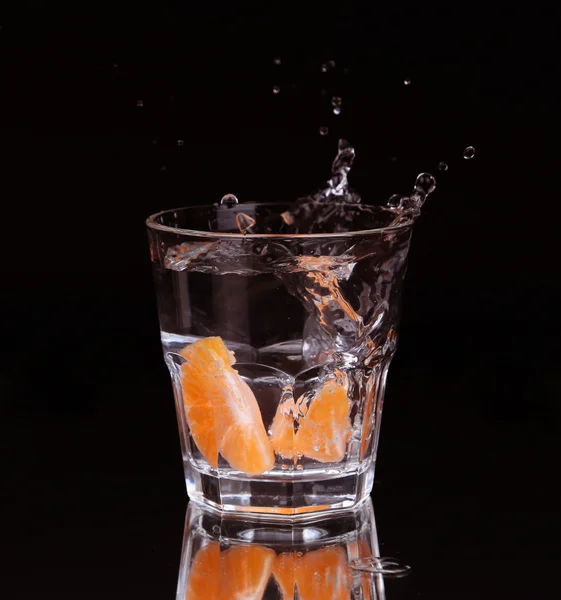 Schijfje citroen spatten in een glas water met een spray van waterdruppels in beweging opgehangen in de lucht boven het glas op een donkere achtergrond. — Stockfoto