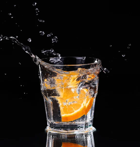 Fatia de limão salpicando em um copo de água com um spray de gotas de água em movimento suspensas no ar acima do vidro em um fundo escuro . — Fotografia de Stock