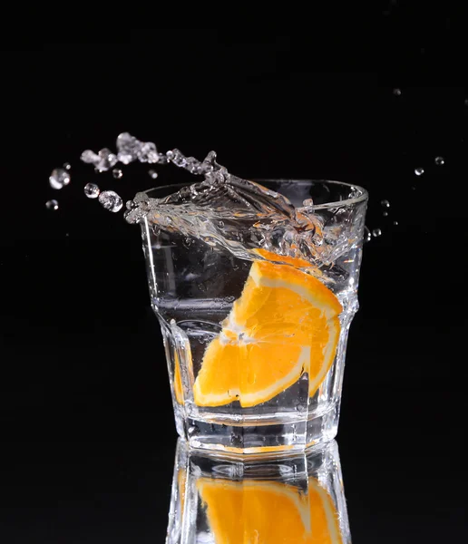 Schijfje citroen spatten in een glas water met een spray van waterdruppels in beweging opgehangen in de lucht boven het glas op een donkere achtergrond. — Stockfoto