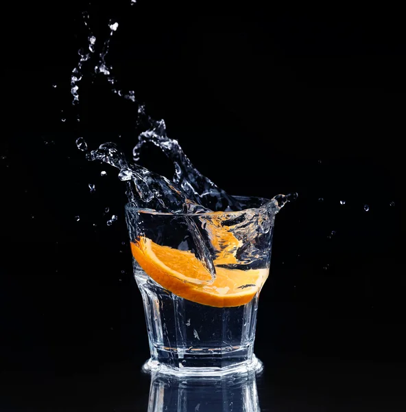 Rebanada de limón salpicando en un vaso de agua con un aerosol de w — Foto de Stock