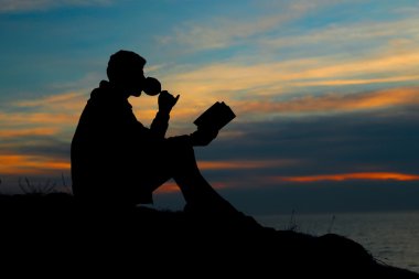 Akşam deniz, okuma kitabı yakınındaki dalgakıran üzerinde oturan bir adam silüeti 