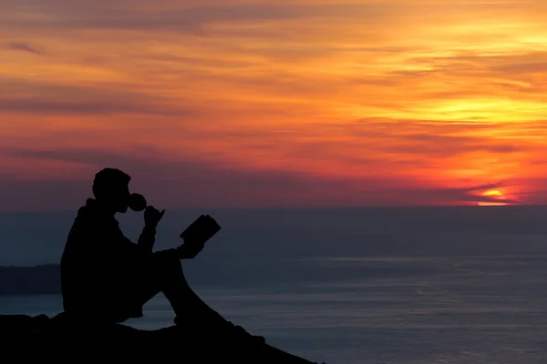 Akşam deniz, okuma kitabı yakınındaki dalgakıran üzerinde oturan bir adam silüeti 