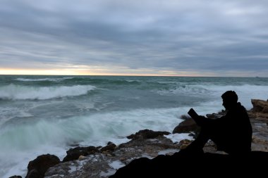dalgakıran akşam deniz, okuma kitabı yanında oturan siluet adam