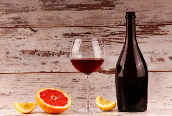 Glas rött vin, en flaska vin och grapefrukt på tavlorna — Stockfoto