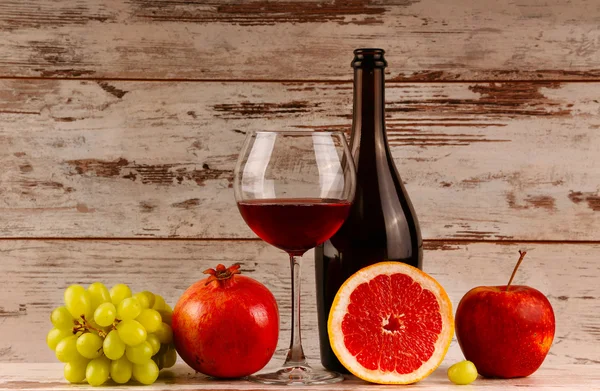 Czerwony butelkę wina na tle drewniane, jabłko i granat — Zdjęcie stockowe