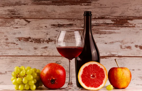 Botella de vino tinto sobre fondo de madera, manzana y granada — Foto de Stock