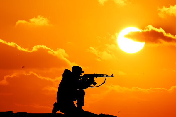 Silhouette shot of soldier holding gun with colorful sky and mountain in background