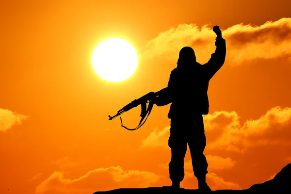 Silhouette lövés katona kezében pisztoly színes ég és a hegy a háttérben — Stock Fotó