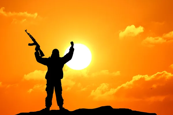 Elinde renkli gökyüzü ve arka planda dağ olan silahlı bir askerin siluet görüntüsü. — Stok fotoğraf
