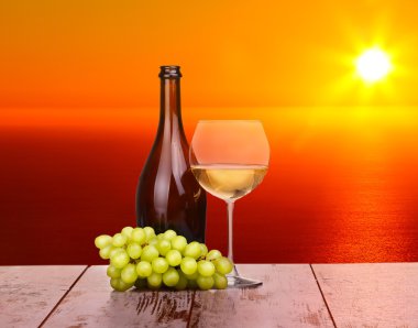 Ahşap bir parça üzerinde günbatımında bir bardak beyaz şarap üzüm