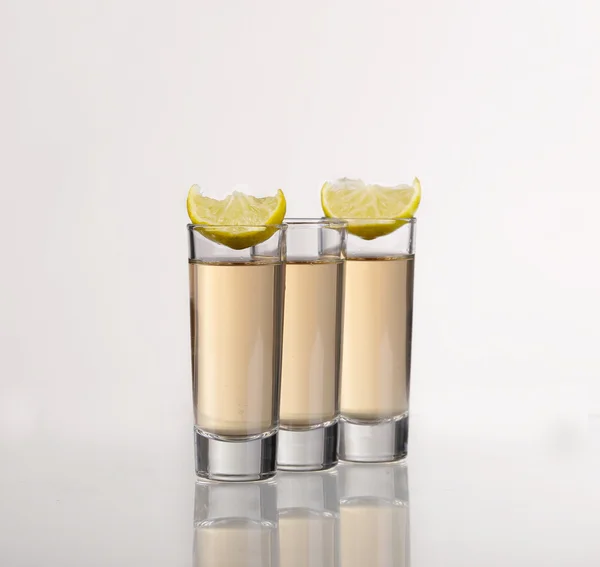 Tre colpi di tequila d'oro con calce su sfondo bianco — Foto Stock