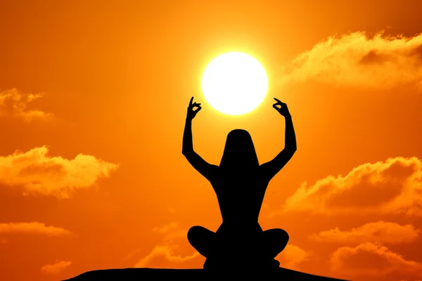 Pratik yoga sırasında günbatımı deniz kenarında kadın silüeti.