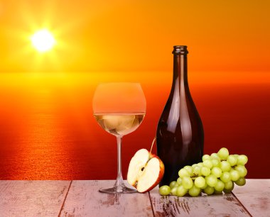 Ahşap bir parça üzerinde günbatımında bir bardak beyaz şarap üzüm