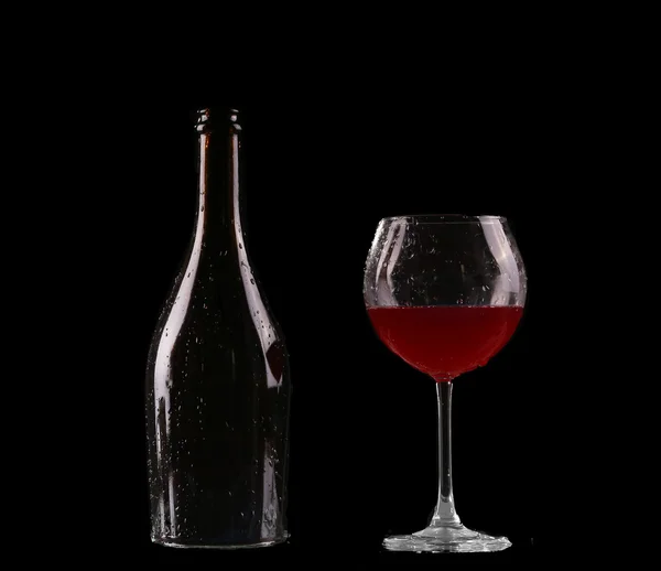 Elegante bicchiere di vino rosso e una bottiglia di vino su sfondo nero — Foto Stock