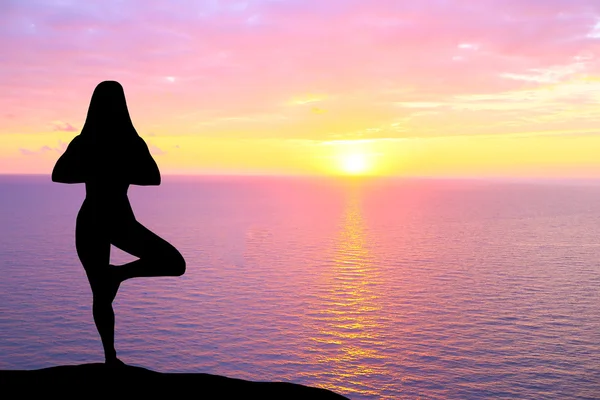 Silhueta de mulher praticando ioga durante o pôr do sol à beira-mar . — Fotografia de Stock