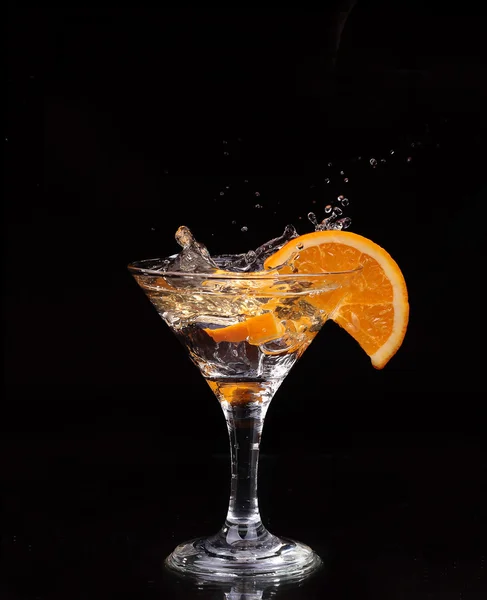 Slice of lemon splashing into a glass of water with a spray of water droplets in motion suspended in the air above the glass on a dark background. — Stock Photo, Image