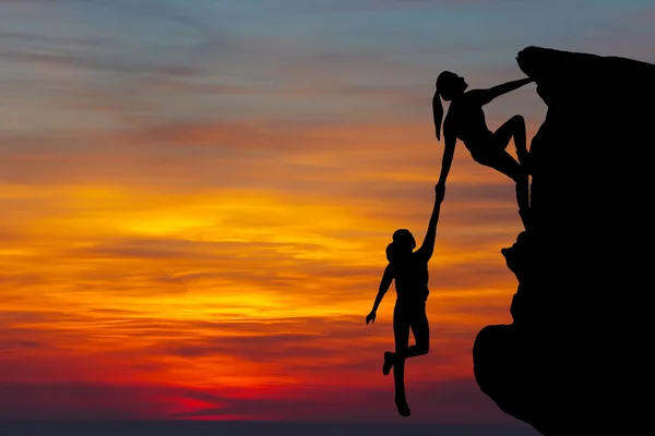 Teamwork couple hiking help each other trust assistance silhouette in mountains, sunset. Teamwork of man and woman hiker helping each other on top of mountain climbing team Stock Picture