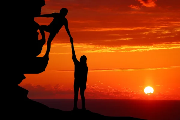 Teamwork couple hiking help each other trust assistance silhouette in mountains, sunset. Teamwork of man and woman hiker helping each other on top of mountain climbing team Royalty Free Stock Photos