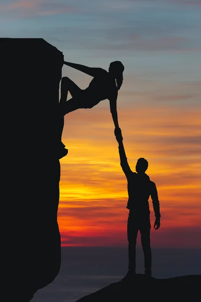 Teamwork couple hiking help each other trust assistance silhouette in mountains, sunset. Teamwork of man and woman hiker helping each other on top of mountain climbing team — Stock Photo, Image