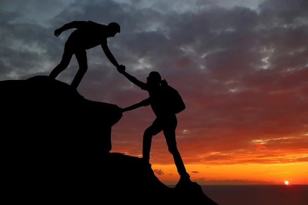 Trabajo en equipo pareja senderismo ayudar a los demás confianza silueta de asistencia en las montañas, puesta del sol. Trabajo en equipo de hombres y mujeres excursionistas ayudándose unos a otros en la cima del equipo de escalada — Foto de Stock