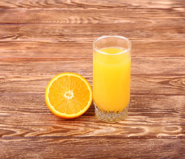 Verre de jus d'orange fraîchement pressé avec moitié d'orange tranchée sur une table en bois — Photo