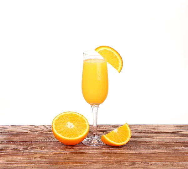 Стакан свежевыжатого апельсинового сока с нарезанным апельсином наполовину на деревянном столе — стоковое фото