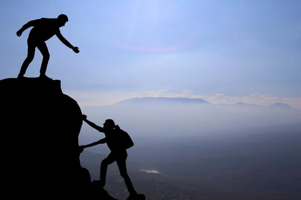 Teamwork couple hiking help each other trust assistance silhouette in mountains, sunset. Teamwork of man and woman hiker helping each other on top of mountain climbing team Stock Image