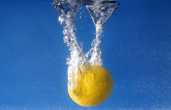 Hele citroen daalde in water tegen blauwe achtergrond met kleurovergang — Stockfoto