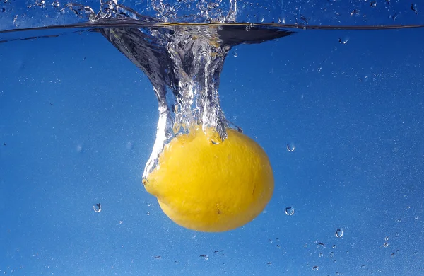 Whole lemon dropped in water against gradient blue background — Stock Photo, Image