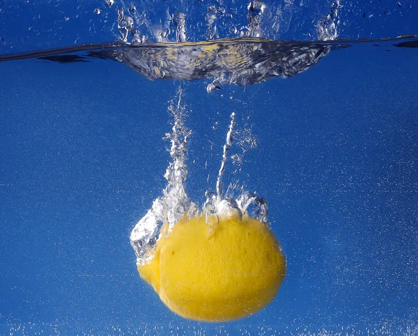 Hele citroen daalde in water tegen blauwe achtergrond met kleurovergang — Stockfoto