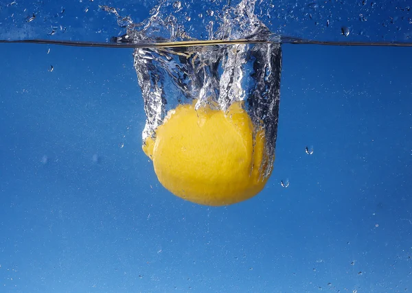 Limón entero caído en agua sobre fondo azul degradado — Foto de Stock