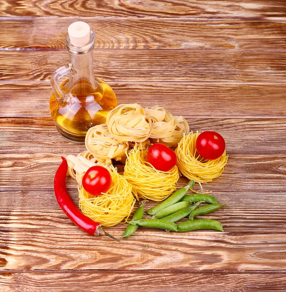 Паста на деревянном фоне с помидорами, салатным перцем, оливковым маслом и перцем — стоковое фото
