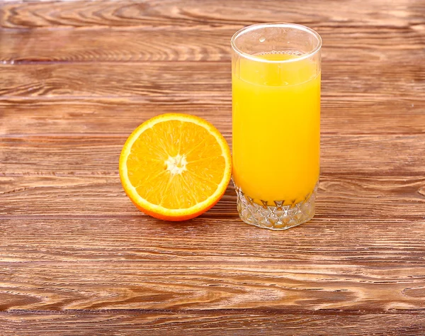 Стакан свежевыжатого апельсинового сока с нарезанным апельсином наполовину на деревянном столе — стоковое фото