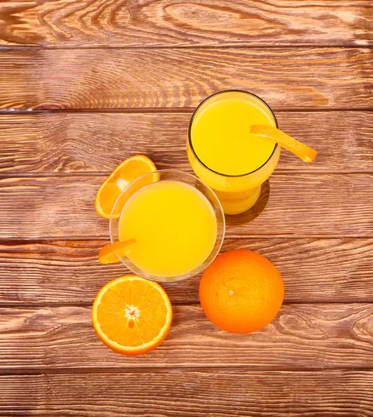 Verre de jus d'orange fraîchement pressé avec moitié d'orange tranchée sur une table en bois — Photo