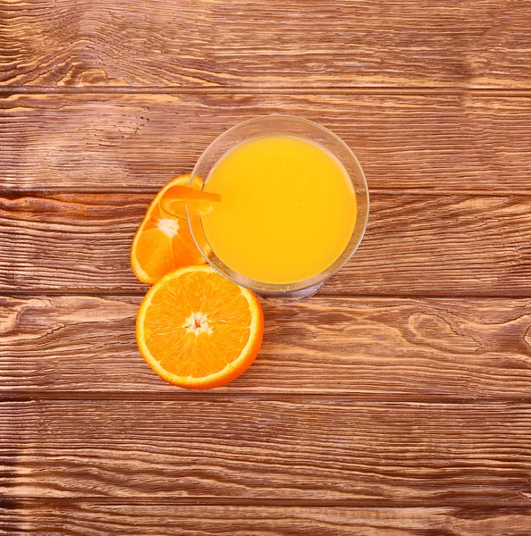 Verre de jus d'orange fraîchement pressé avec moitié d'orange tranchée sur une table en bois — Photo