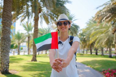 Abu Dabi silueti üzerinde BAE 'nin küçük bayrağını taşıyan kadın Abu Dabi' de gezinti güvertesi. Birleşik Arap Emirlikleri, Orta Doğu. Göçmenlik, öğrenci eğitimi ve Arap Emirlikleri vatandaşlık kavramı