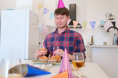 Adam geleneksel doğum günü pastası yerine mumlarla süslenmiş dört kekle kutluyor. Gülümseyen ve neşeli, sıcacık ve eşsiz kutlamalardan zevk alıyor, sıcak ve unutulmaz bir an yaratıyor..