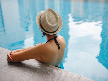 Kuala Lumpur Oteli 'nde havuz başında dinlenen Asyalı genç bir kadın. Etrafı gökdelenlerle çevrili, hareketli şehir ortamında boş vakitlerin tadını çıkarıyor..