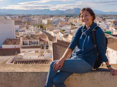 Denia, Alicante, İspanya 'da tarihi şatoyu keşfeden genç bir kadın, aşağıdaki kasabanın manzarası, daha serin mevsim arkaplanlarına karşı. Tarihin ve sükunetin zamansız ortamında harmanlanması.