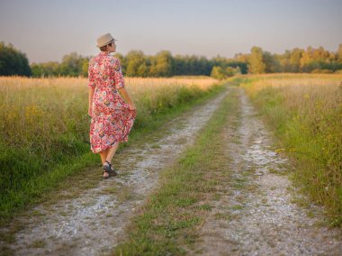 Yaz sonlarında Avrupa 'nın pitoresk alanlarında yürüyen genç bir kadın. Altın güneş ışığı, yemyeşil yemyeşil ve sakin kırsal atmosfer huzurlu bir kırsal alan yaratır..