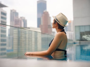 Kuala Lumpur Oteli 'nde havuz başında dinlenen Asyalı genç bir kadın. Etrafı gökdelenlerle çevrili, hareketli şehir ortamında boş vakitlerin tadını çıkarıyor..