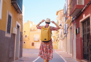 İspanyol kıyı kasabası La Vila Joiosa 'nın renkli sokaklarında gezen kadın. Güneşli kış atmosferi Akdeniz mimarisinin cazibesini ve sakin sahil yaşamını ön plana çıkarıyor.
