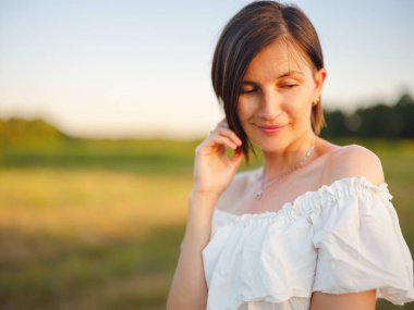 Hırvatistan 'da yaz günbatımında beyaz elbiseli güzel bir kadın, sıcak güneş ışığı, romantik akşam havası, doğal kırsal atmosfer, yumuşak rüzgar ve huzurlu manzara.