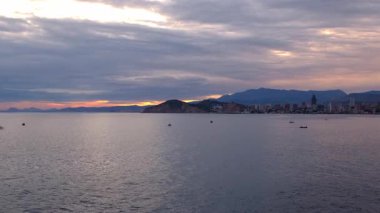 Cala Tio Ximo kıyı şeridi Aralık akşamında ele geçirildi. Sakin kış denizi, yumuşak gün batımı parıltısı, Benidorm yakınlarındaki küçük adanın huzurlu manzarası. Sessiz doğal güzellik, insan yok, sadece deniz ve gökyüzü..