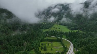Avusturya sınırına yakın Slovenya 'daki Katolik kilisesinin yanından geçen İHA, bulutlu yaz gününde dramatik dağ arkaplanı ve yeşil ormanla sinematik seyahat perspektifi oluşturuyor.