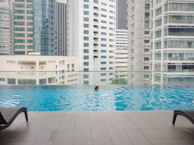 Kuala Lumpur Oteli 'nde havuz başında dinlenen Asyalı genç bir kadın. Etrafı gökdelenlerle çevrili, hareketli şehir ortamında boş vakitlerin tadını çıkarıyor..